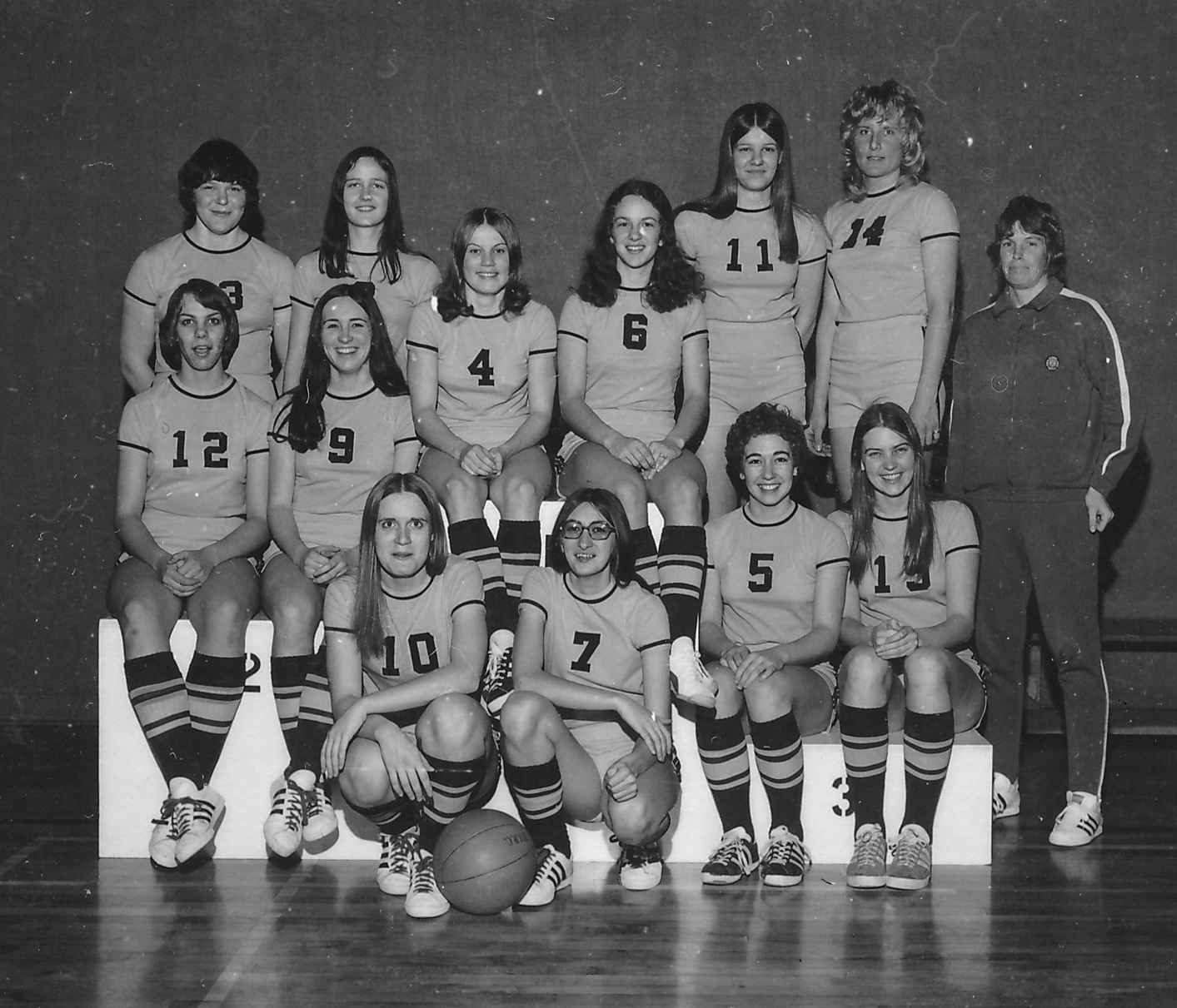 Smiling individuals in archival black and white image of women's basketball team.